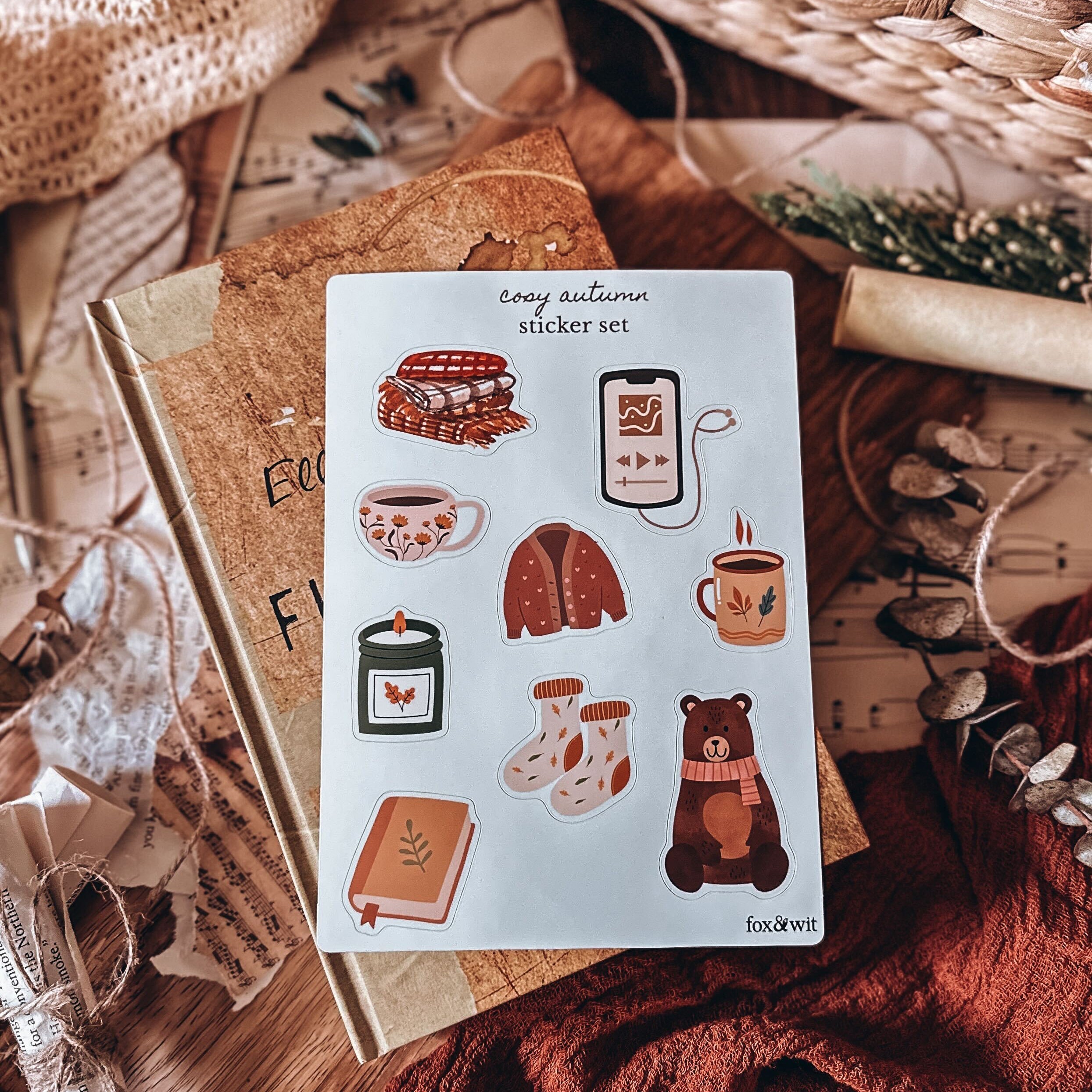stack of books sitting on a decorated background. On top features a sheet of sticker featuring cosy autumn items.