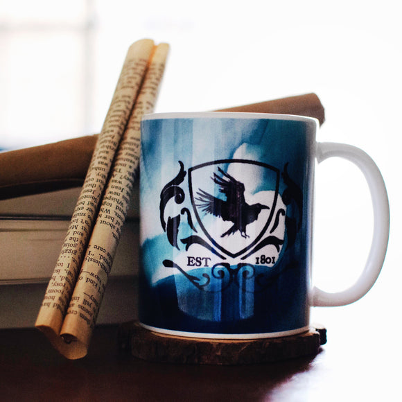a mug with greenish blue watercolor swirls with a raven crest in the center