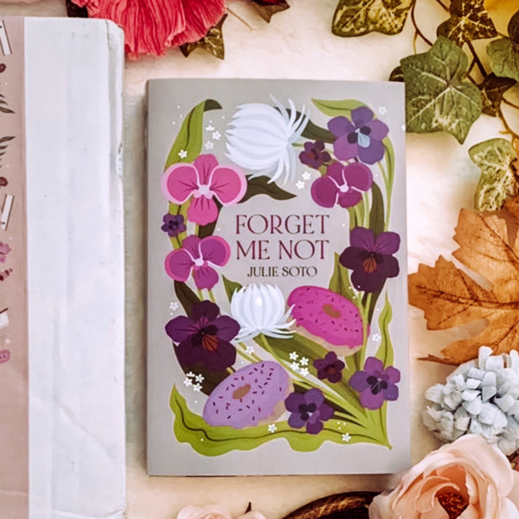 A book cover with the title 'Forget Me Not' by Ali Hazelwood, featuring a floral design with various flowers and leaves on a grey background.