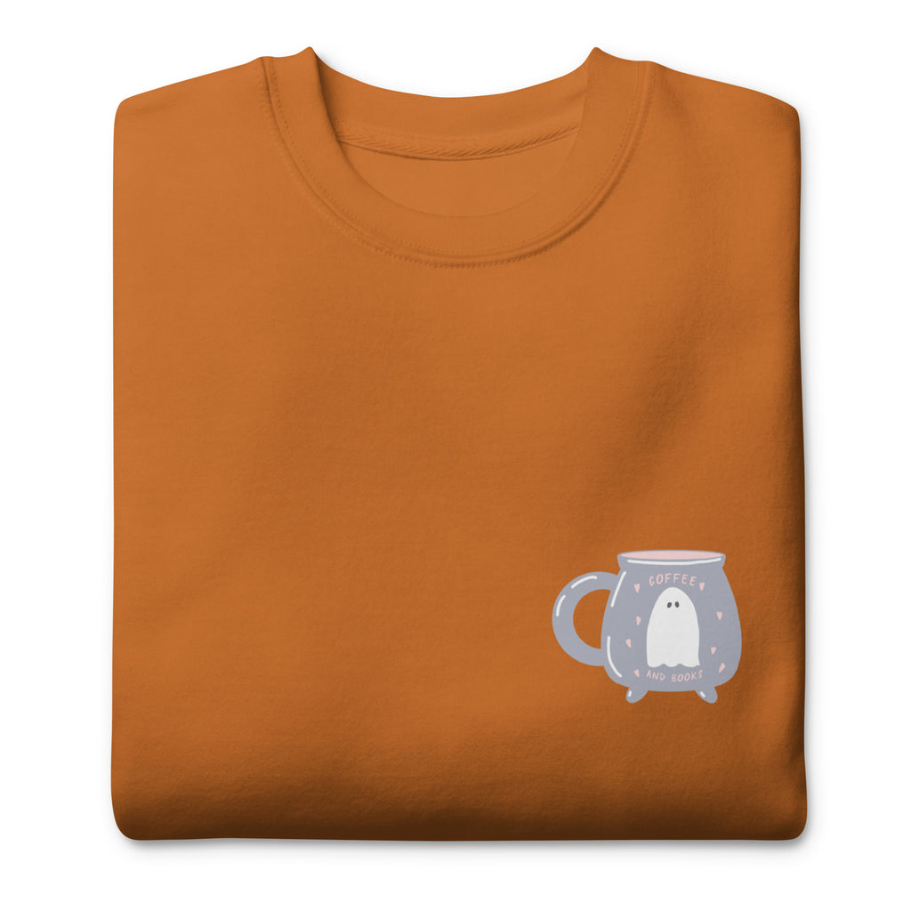 Design featuring a ghost inside of a cauldron shaped mug on the right hand side of a burn orange colored sweater. On a white background.