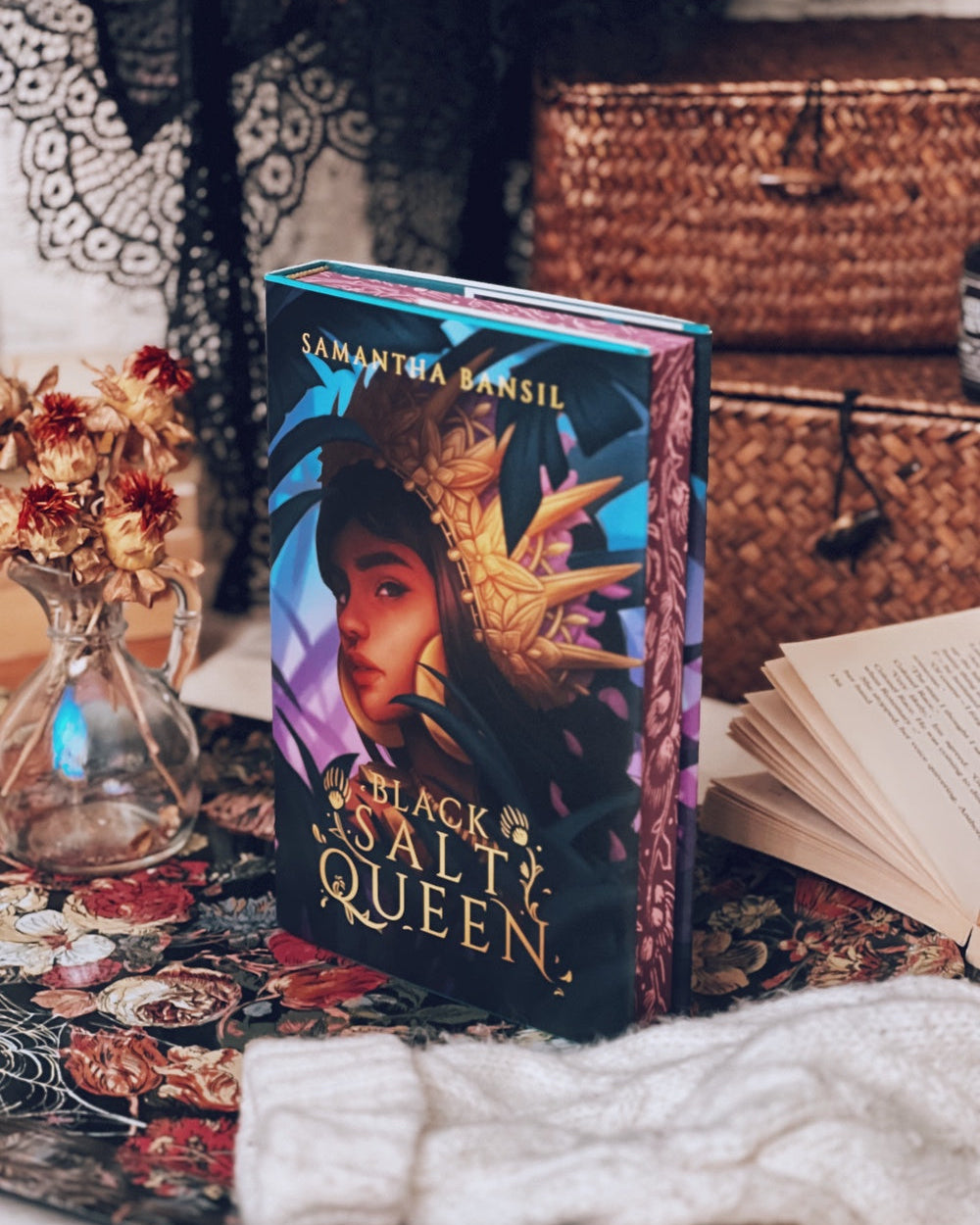 Book titled 'Black Salt Queen' by Samantha Bensil on a decorative surface with flowers and a woven basket.