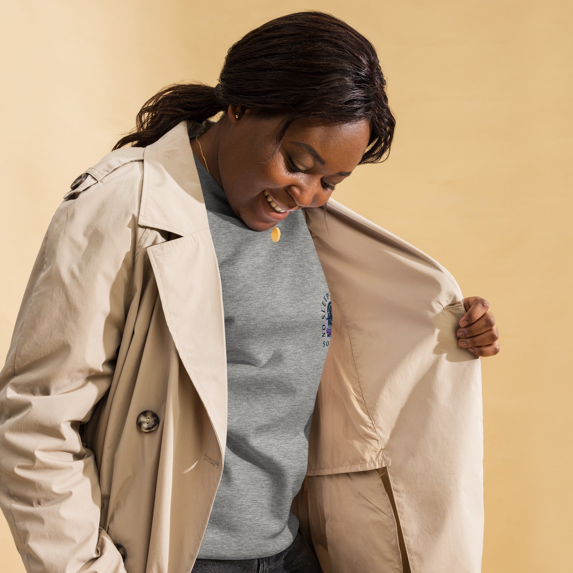 Image of a Black woman wearing a grey sweatshirt  with the design "no sleep reader society" and a cream trench coat.