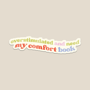 This Overstimulated and Need My Comfort Book sticker and  features soft pastel rainbow text with a retro vibe