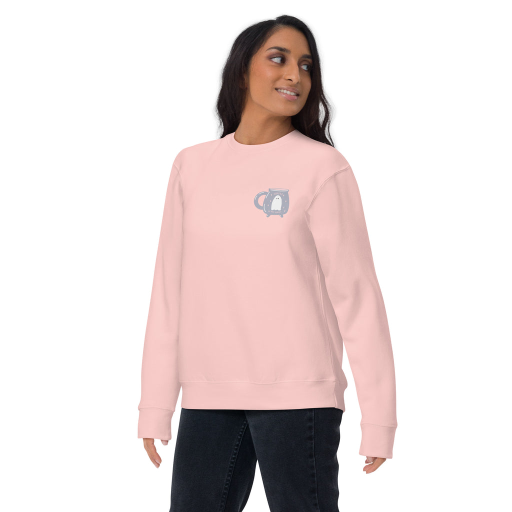 Woman wearing a light pink sweatshirt with a pocket design featuring a ghost inside a cauldron shaped coffee mug with text that reads "coffee and books" on a white background