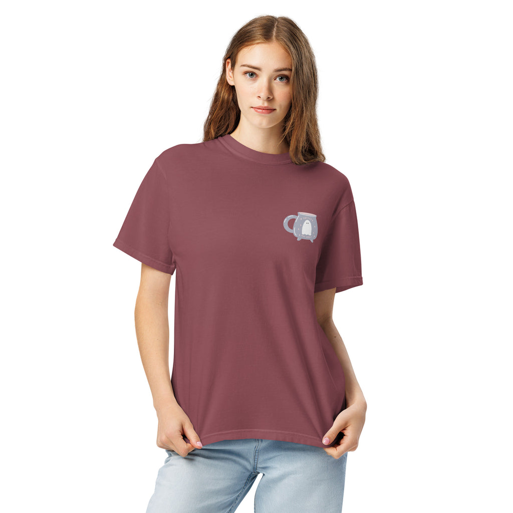 Woman wearing a maroon t-shirt with a design that features a ghost inside of a cauldron shaped mug on a white background
