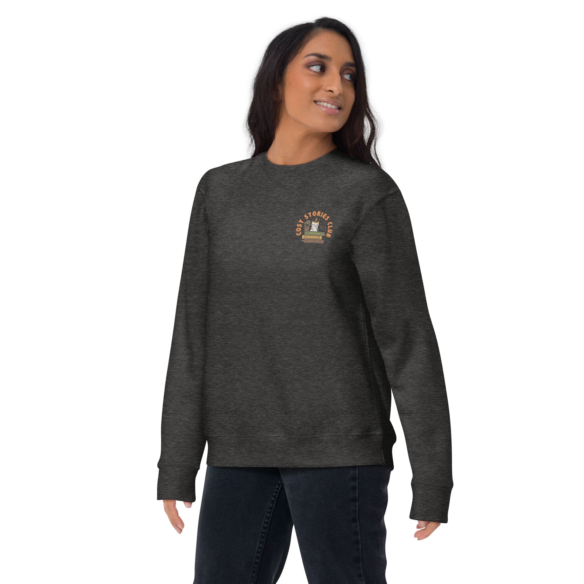 Woman wearing a dark gray sweatshirt with a pock design that reads cosy stories club on a white background