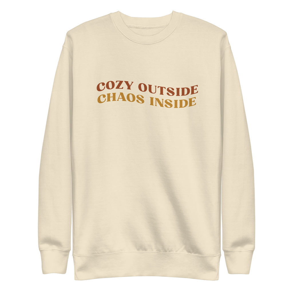 cream sweater with the words "cozy outside chaos inside" written in the center. displayed on white background.