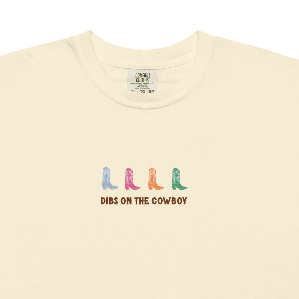 Beige t-shirt with colorful cowboy boots and text that reads "dibs on the cowboy". Shown on a white background
