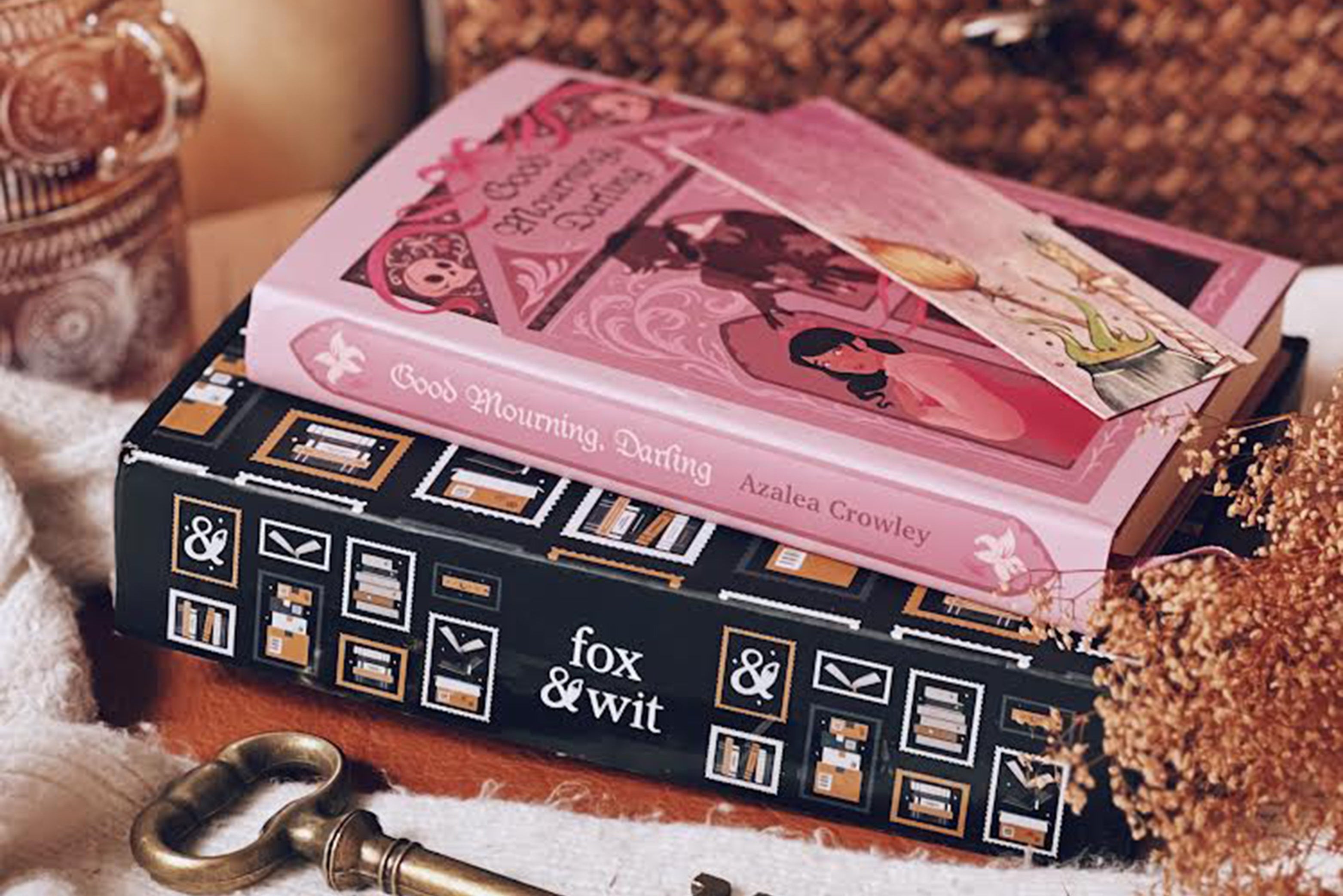 Book with pink cover titled 'Good Morning, Darling' by Azalia Crowley, placed on a black book with 'fox & wit' branding, next to a key.